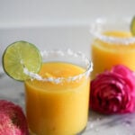 mango ginger margarita in a clear salt rimmed glass with lime garnish and pink flowers on marble top.
