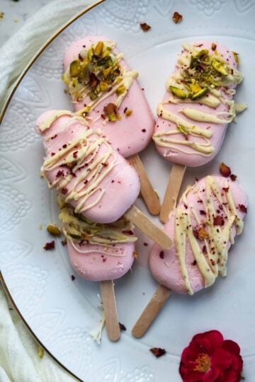 rose milk popsicles with white chocolate cardamom drizzle and pistachios