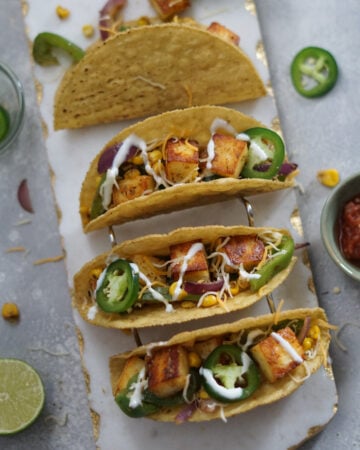 Assembled paneer tacos with jalapenos and lime spice crema on a marble board.