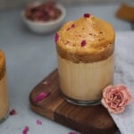 rose dalgona coffee with rose petals on a wooden board on gray surface