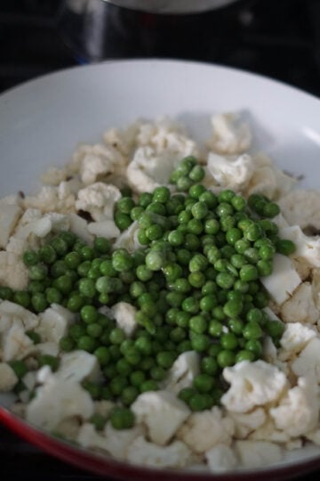 Cauliflower and peas added to white pan on stove.