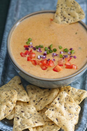 Tandoori queso in a steel tray with chopped veggies on top and tortilla chips on the side.