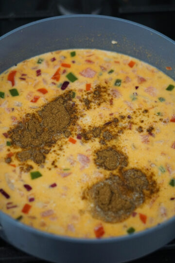 Spices added to tandoori queso in gray pan.