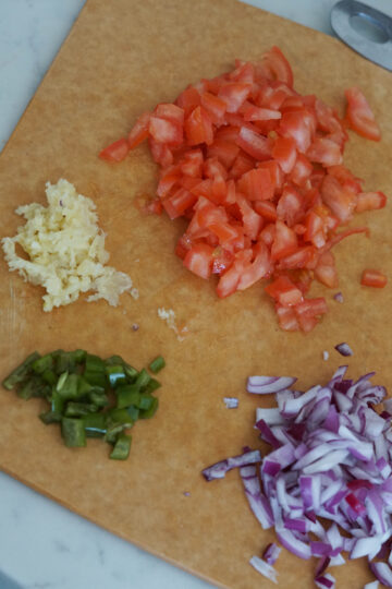Minced garlic and chopped onions, tomatoes and jalapenos on a cutting board.