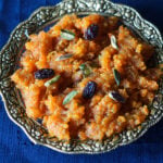 vegan gajar ka halwa in a gold trim bowl with raisins and pistaschios