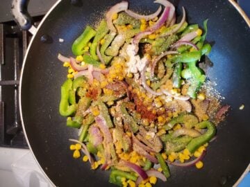 Sliced onions, bell peppers and corn in a non-stick pan with spices.