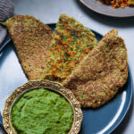 Vegetable moong dal pudla on a blue plate with green cilantro chutney on the side.