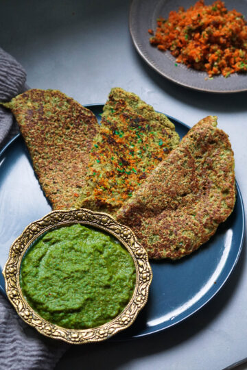 Vegetable moong dal pudla on a blue plate with green cilantro chutney on the side.