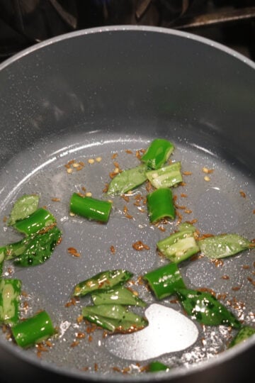 Heated oil in a pan with jeera seeds, curry leaves and green chillies.
