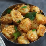 Sukhi bhaji a farali dry potato bhaji in a silver bowl with curry leaves on a gray dish.