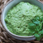 Cilantro chutney in a bowl with a coriander leaf