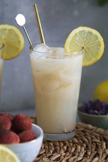 litchee juice lemonade in a glass topped with a lemon slice and lychees in a white bowl on the side.