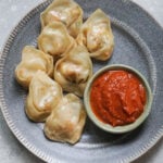 Paneer momos on a gray plate with chutney in a small bowl to the side.
