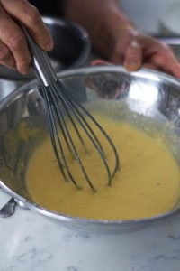Whisking khaman dhokla batter ingredients in a steel bowl.