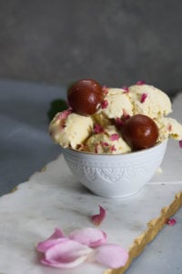 Gulab jamun ice cream scoops with gulab jamuns and rose petals with pink roses to the side.