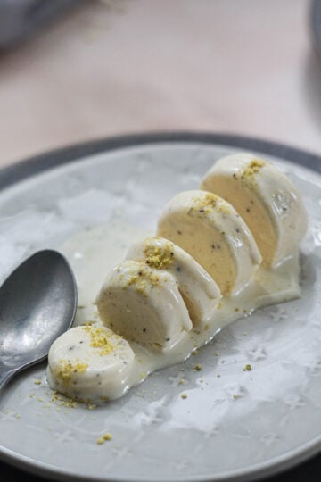 Kulfi with khoya or mawa on a white plate with pistaschio sprinkled on top with a spoon to the side.