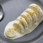 Mawa kulfi cut in slices on a gray plate with ground pistaschios sprinkled on top.