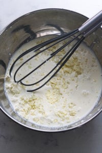 Khoya whisking into heavy cream and condensed milk in a steel bowl.