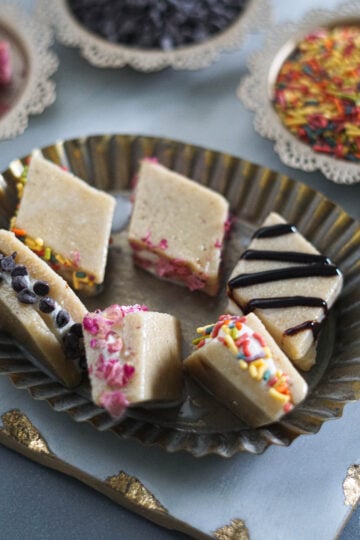 Kaju katli pieces sandwiching ice cream with various topins such as sprinkles and chocolate chips.