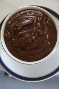 Tamarind chutney in a white bowl on a white plate rimmed blue.