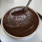 Imli ki chutney in a bowl with a silver spoon on a white plate with a blue rim.