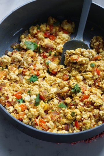 Paneer bhurji ready to eat in a non-stick pan with a serving spoon.