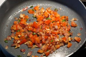 Veggies for paneer bhurji sauteed in a pan.