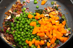 Peas and carrots added to spices in pan.