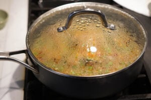 Covered pot of quinoa upma cooking on stovetop.