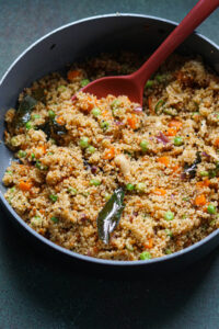 Quinoa upma, one pot meal ready in a pan with a serving spoon.