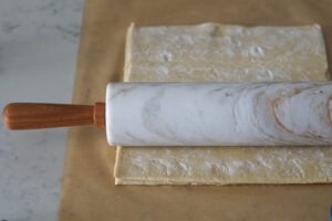 Puff pastry sheets being rolled out with a marble rolling pin on parchment paper.