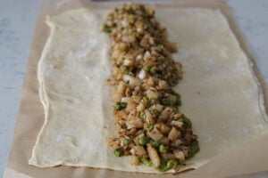 Samosa filling spread on top of green chutney in center of puff pastry sheet.