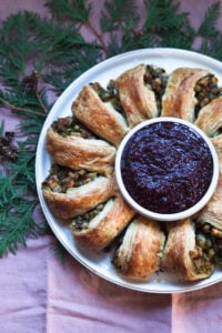 Baked samosa wreath with cranberry chutney in center in a bowl laid atop greenery.