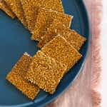Sesame Chikki or Til Chikki squares in a half circle on a blue plate resting on a pink fringe cloth.