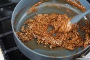 Sesame seeds added to melted jaggery being mixed in a pan.