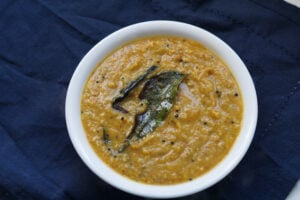 Roasted chana dal chutney in a white bowl with curry leaf on top.