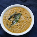 Roasted chana dal chutney in a white bowl with curry leaf on top.