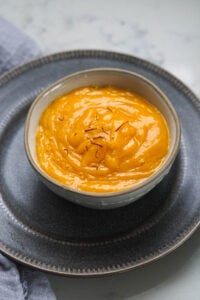 Mango ras or aamras in a small bowl with a spoon, topped with saffron threads.