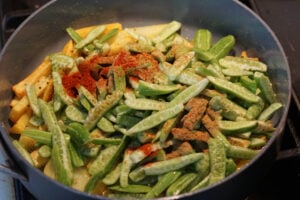Tindora added to potatoes in pan.