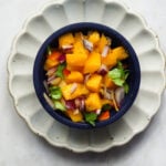 Mango habanero salsa in blue bowl resting on a white fluted plate.