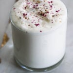 Sweet lassi in a glass with crushed rose petal garnish.