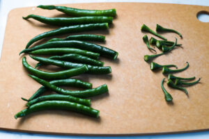 Green chillies with stem chopped off on a cutting board.