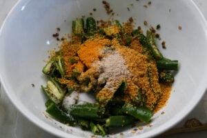 Spices added to green chilies in a bowl.