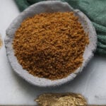 Roasted cumin seed powder in a gray plate with a green cloth to the side.