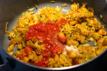 Crushed tomatoes added to cabbage shaak in pan.