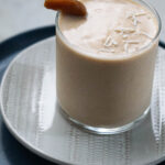 Chikoo milkshake on a plate with coconut shred garnish and a slice of chikoo.