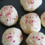 Rose coconut ladoos on a gray plate garnished with rose petals.