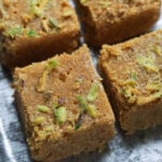 Mohanthal pieces with pistachio garnish on a steel tray.