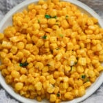 Masala corn in a white plate on gray cloth.