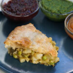 Samosa pie piece on a blue plate with chutneys on the side.